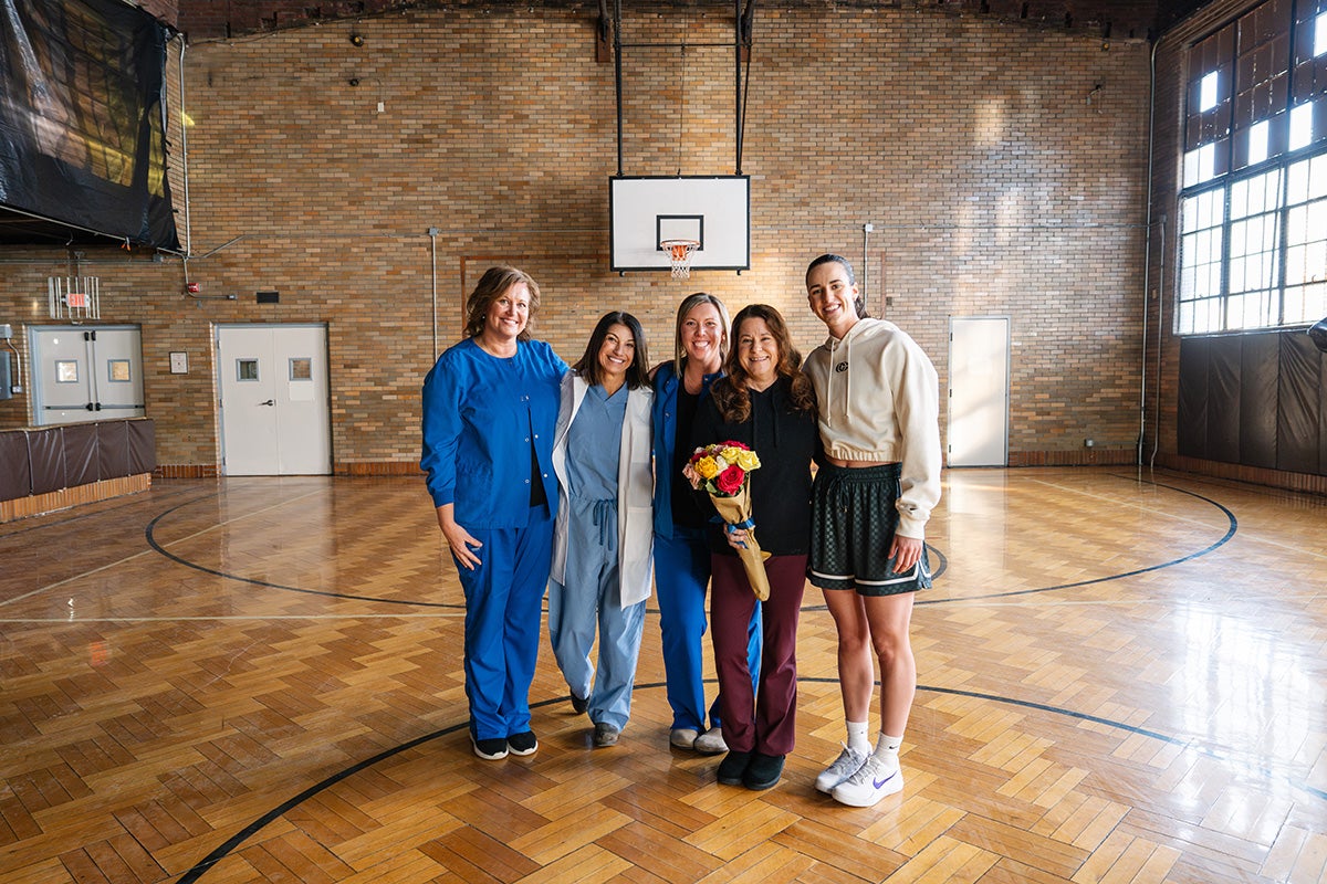 Group of women standing with Caitlin Clark on a basketball court holding flowers.