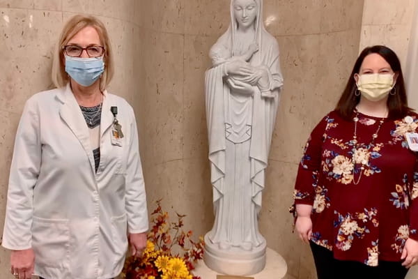 Dianna Speer and Sarah Smart standing by a statue inside Ascension Via Christi