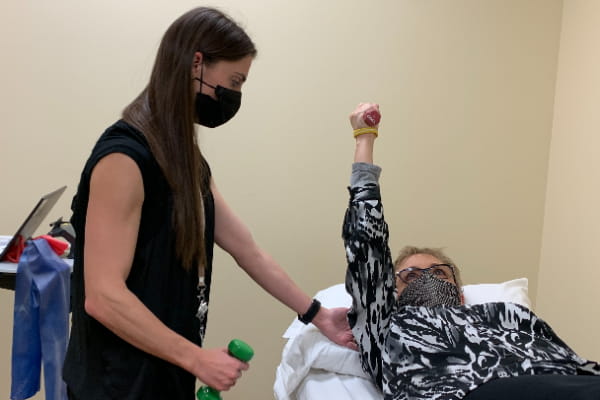 Patient lifting arm during physical therapy with occupational therapist assisting