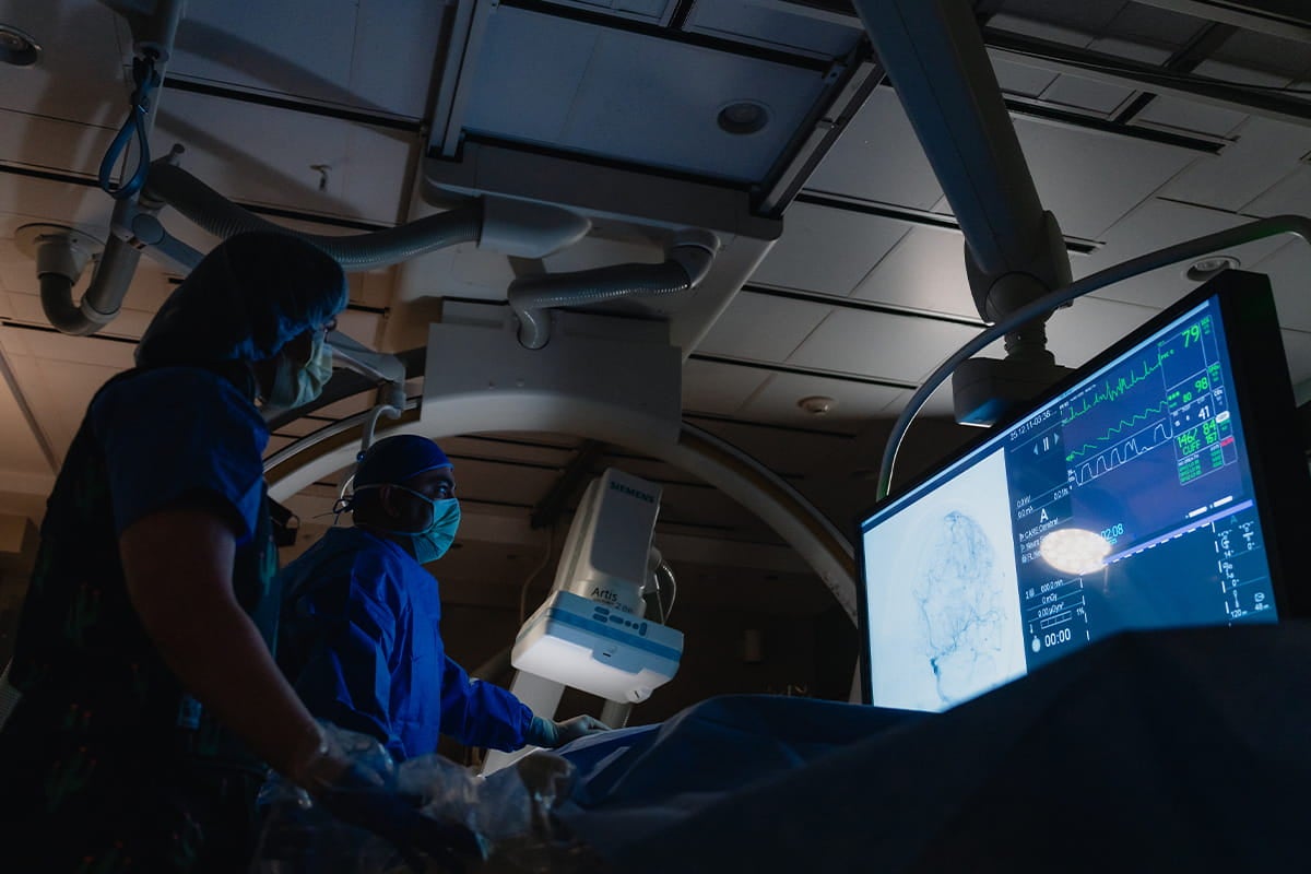 Two surgeons in an operating room review a brain scan on a large monitor during a minimally invasive neurological procedure.