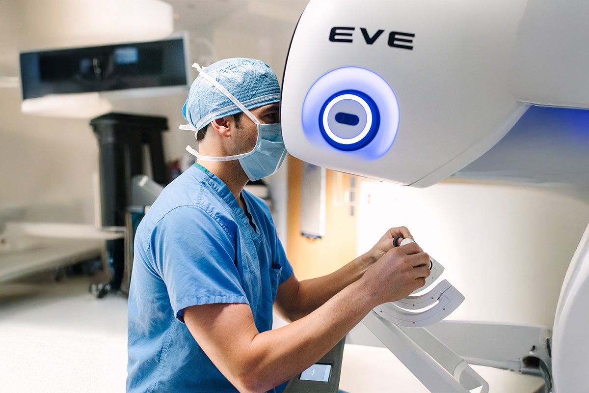 Healthcare professional in scrubs and a surgical cap operates an EVE  device in a clinical setting.