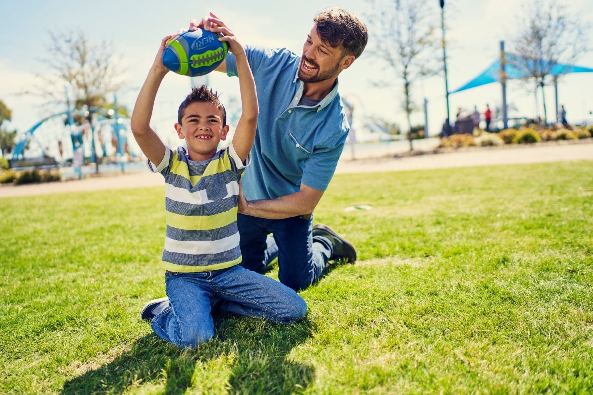 man holding football with boy in a grassy park