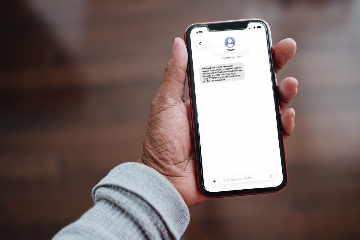 Hand holding a smartphone displaying an Ascension text message enrollment confirmation.