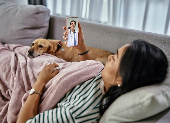 A woman laying on the couch, looking at her mobile phone during a virtual visit with a provider.
