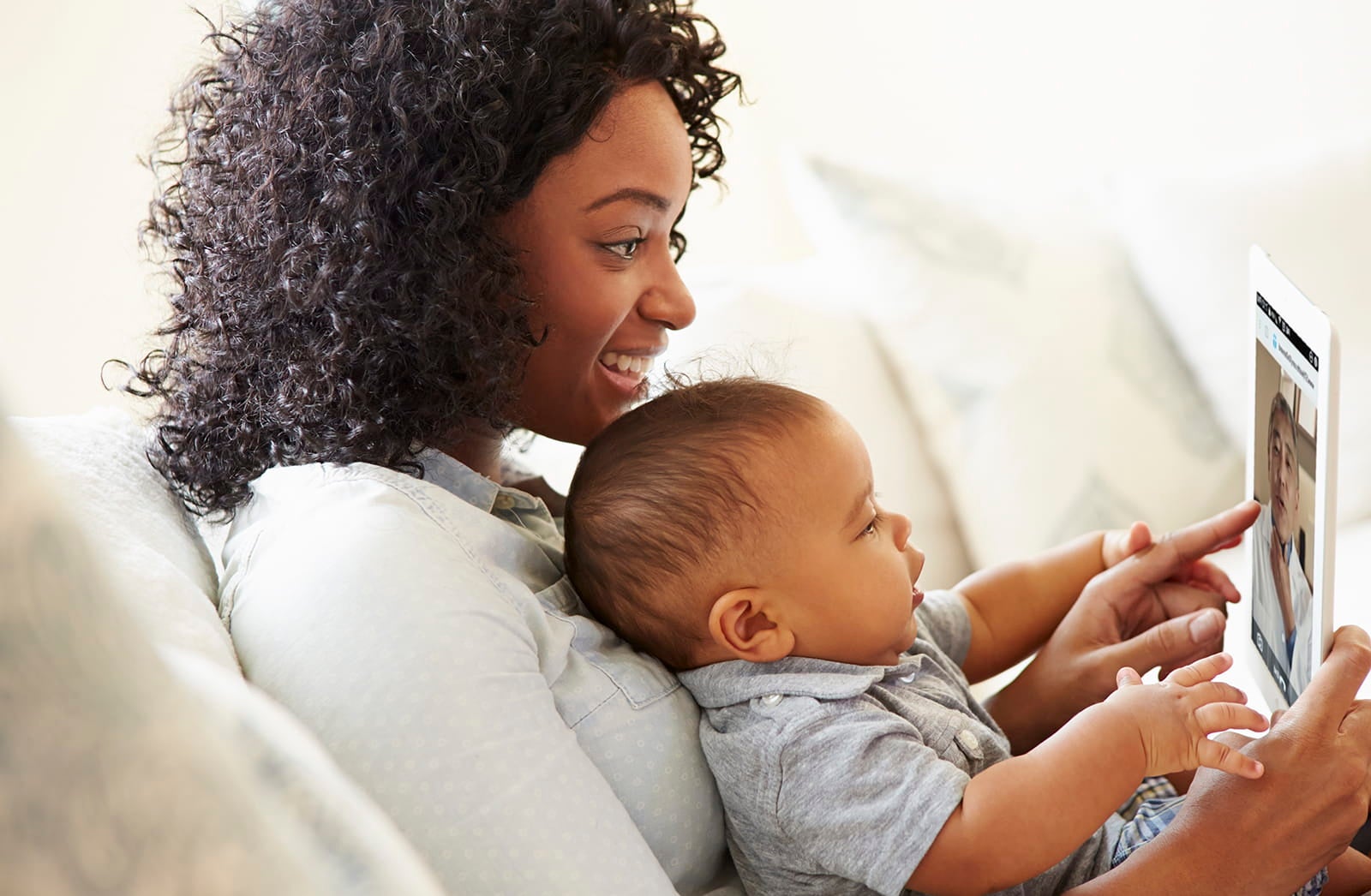Young woman receiving virtual care from her doctor while holding her infant.