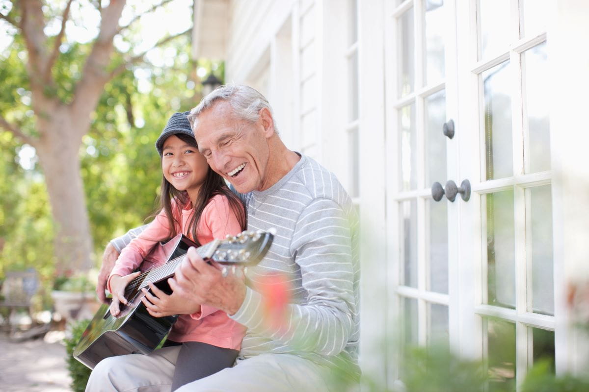 Elderly man plays guitar on the patio with his granddaughter