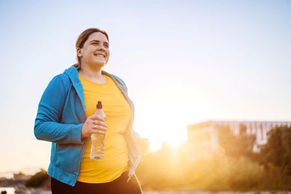 woman smiling while running with a water bottle in her hand