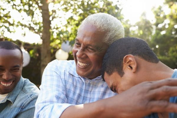 Grandfather, father, and son hugging outdoors