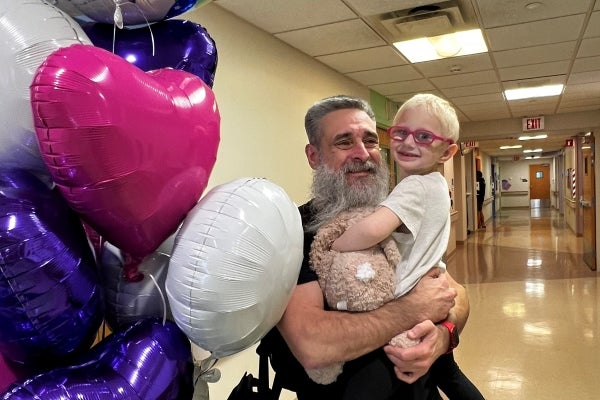 father holding daughter at Peyton Manning Children's Hospital with pink, purple and white balloons next to them
