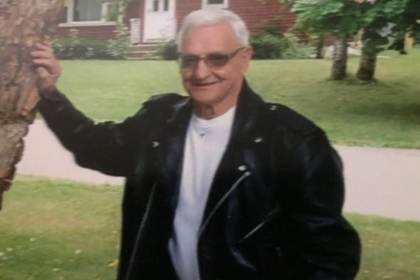 An elderly man poses for a photo in a leather jacket