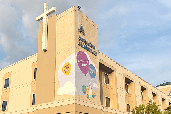 Exterior view of an Ascension Ascension St. Vincent's Clay County with a large cross on the facade, featuring banners and the Ascension logo against a partly cloudy sky.