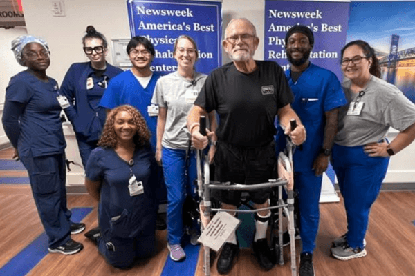 Mark stands with a walker surrounded by members of his rehabilitation care team.