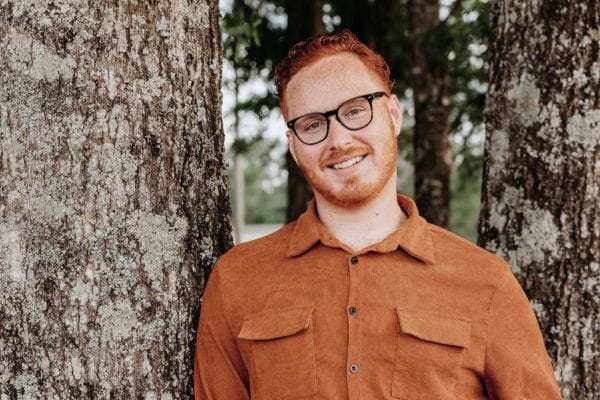 Patient Christopher standing by a tree