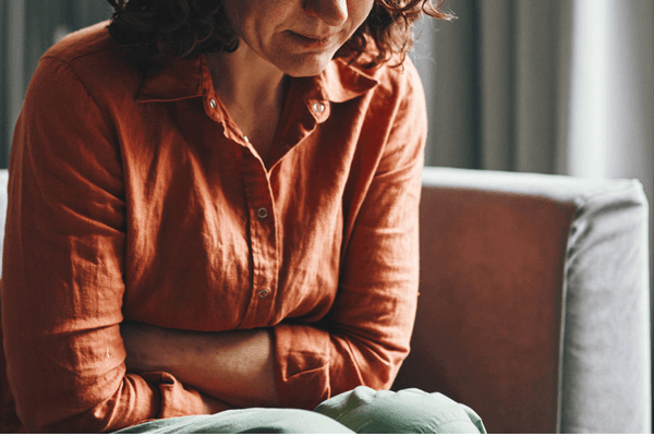 A woman sitting crosses her arms and is in discomfort.